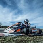 Go-kart driver demonstrating expert cornering technique on a race track, showcasing proper racing line and body positioning.
