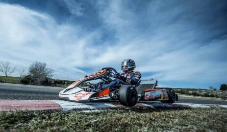 Go-kart driver demonstrating expert cornering technique on a race track, showcasing proper racing line and body positioning.